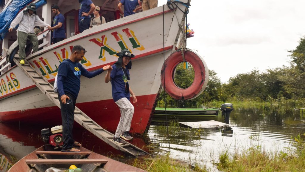 Pessoas descendo de um barco, e um rapaz auxiliando